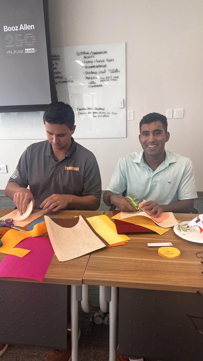 Two volunteers cutting and assembling colorful felt costume pieces at a table.