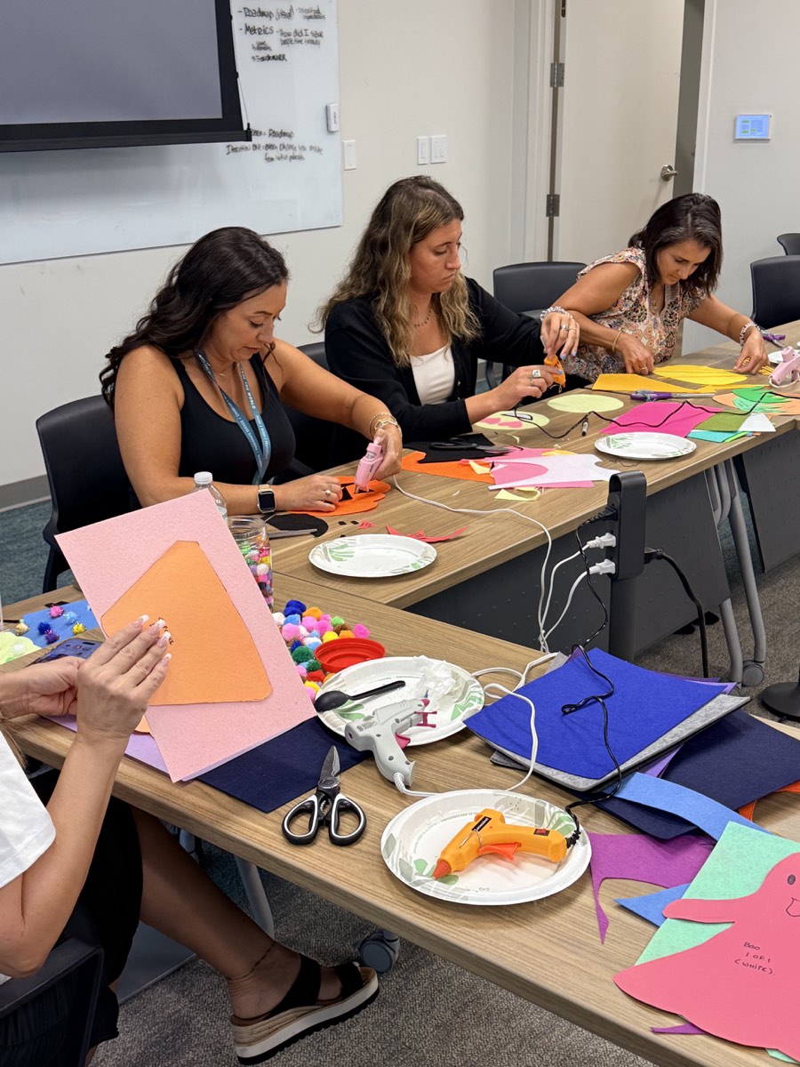 Three volunteers working together to assemble colorful felt costumes at a shared craft table.